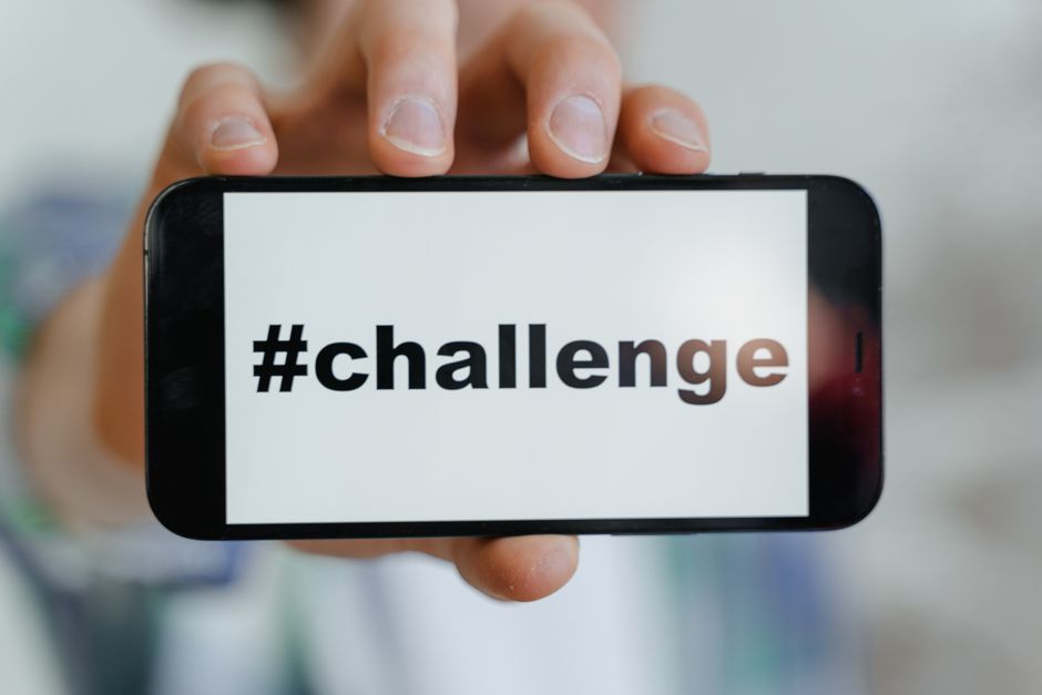 Pessoa segurando um smartphone exibindo a palavra '#challenge' em destaque, simbolizando um convite para superar obstáculos e testar limites.