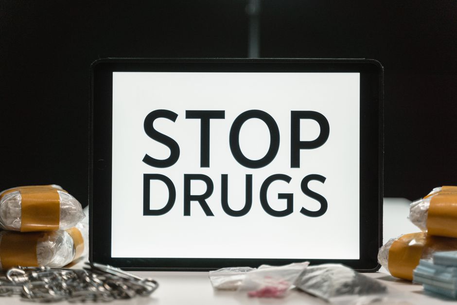 Imagem de um tablet com a mensagem 'Pare com Drogas' ao centro, cercado por pequenas porções de drogas e itens relacionados ao combate às drogas.