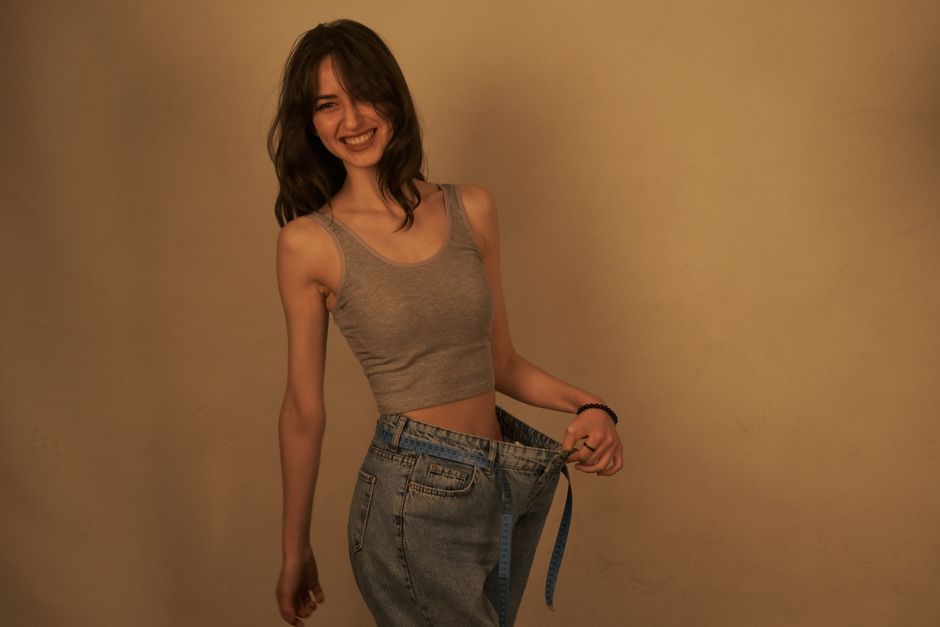 Jovem sorridente mostrando perda de peso com calça folgada, simbolizando transformação física e bem-estar.