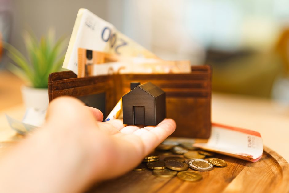 Imagem de uma carteira de dinheiro com uma casa em miniatura, simbolizando investimentos ou economia imobiliária.
