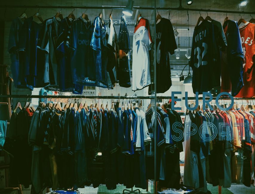 Vitrine de loja de roupas esportivas com camisetas e uniformes de times de futebol variados em destaque.