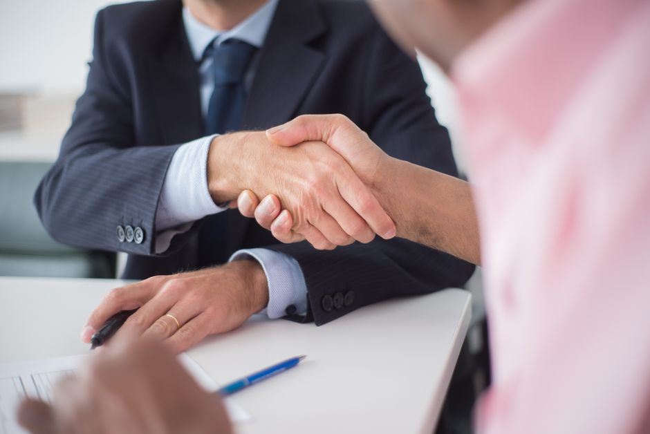 Imagem de duas pessoas fechando um acordo com um aperto de mãos, simbolizando parceria ou negociação empresarial.