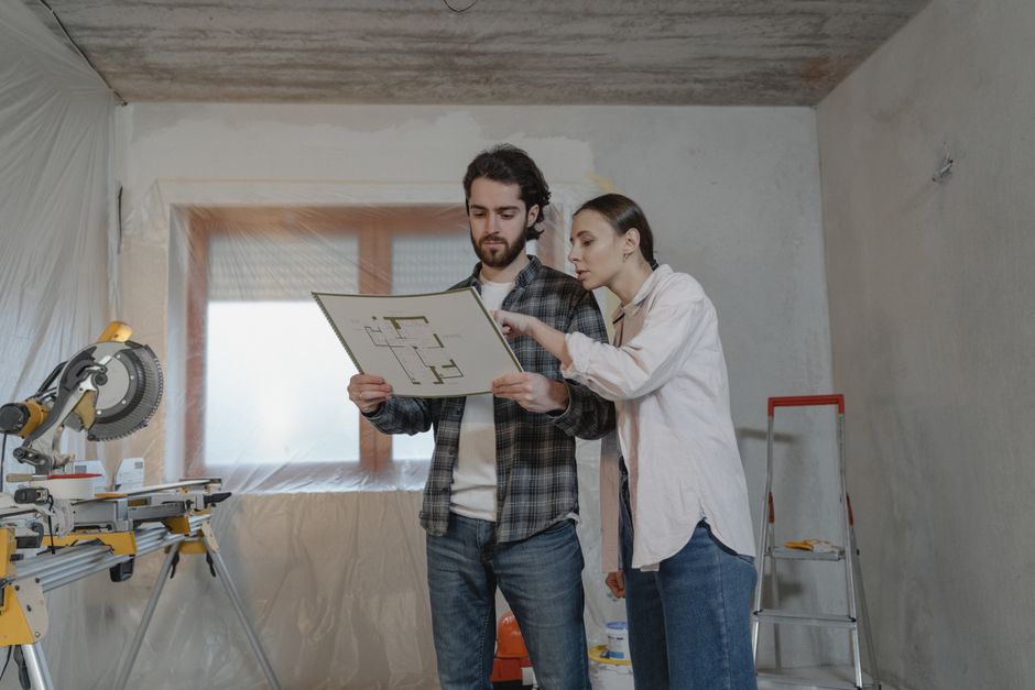 Homem e mulher discutindo projeto de construção em um ambiente de reforma ou obra, com ferramentas de marcenaria ao lado.