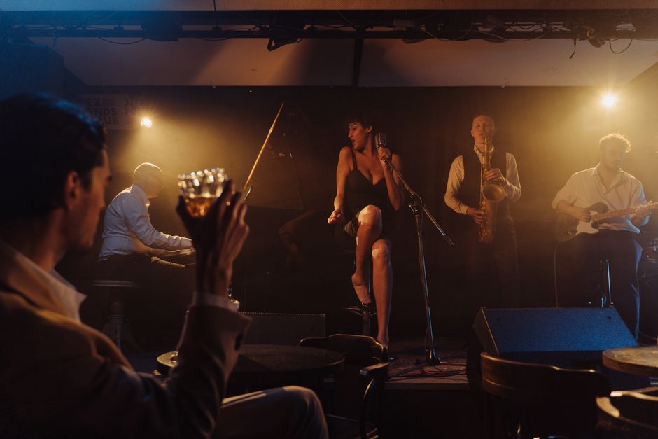 Vocalista de jazz apresentando-se em um show ao vivo, acompanhado por uma banda durante uma apresentação íntima em um ambiente escuro e aconchegante.