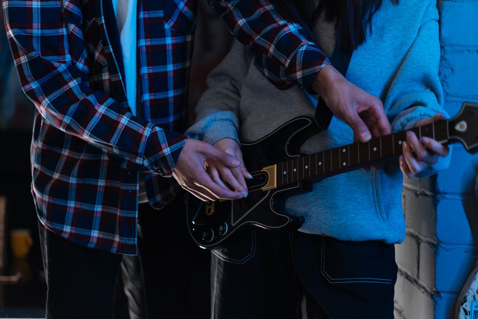 Duas pessoas aprendendo a tocar guitarra em um ambiente interno, evidenciando colaboração e ensino musical.
