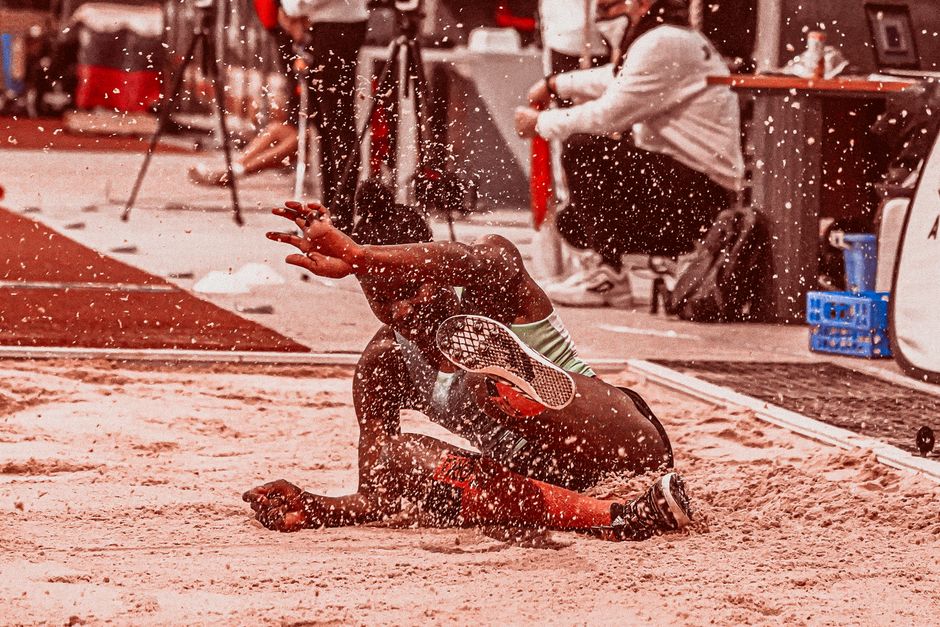 Atleta de vôlei de praia caindo na areia durante uma partida, representando intensidade e habilidade esportiva.