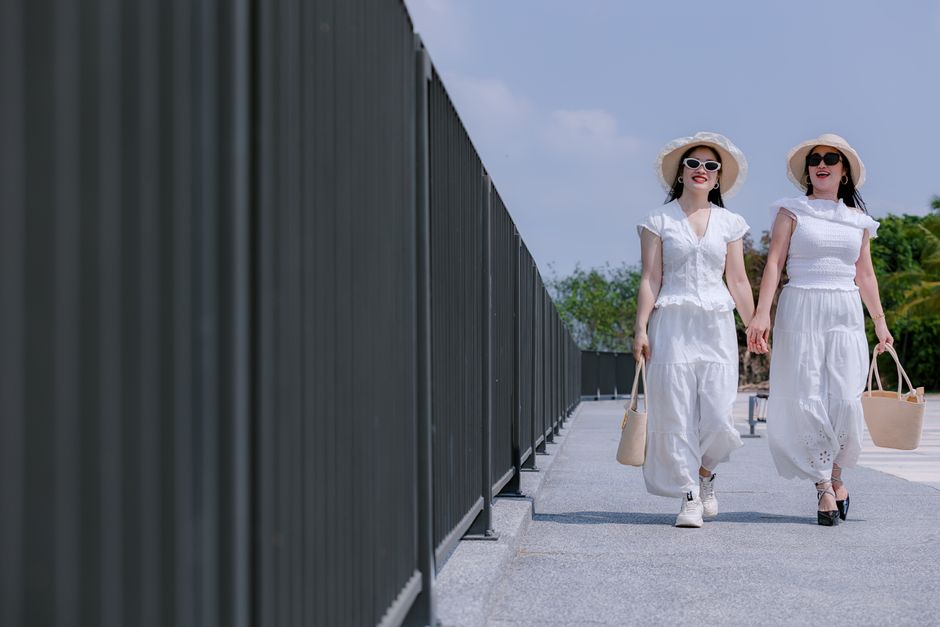 Duas mulheres desfrutando de um dia ensolarado em um ambiente ao ar livre, vestindo roupas brancas elegantes e chapéus de palha, simbolizando liberdade e bem-estar.
