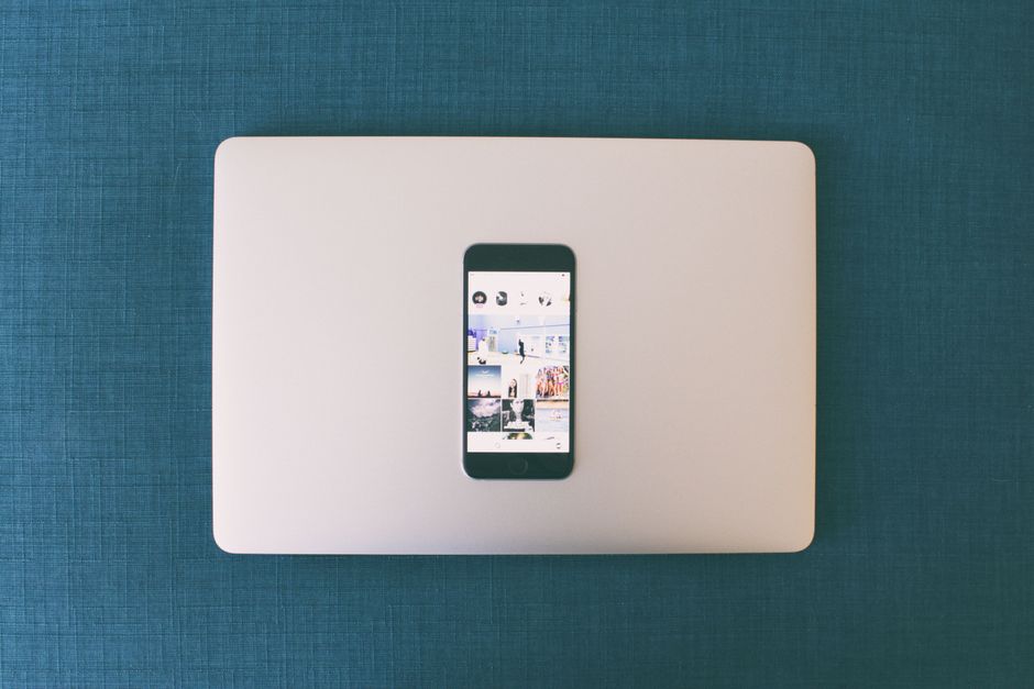 Imagem de um smartphone colocado sobre um laptop branco em uma superfície azul, simbolizando conexão digital e tecnologia móvel.