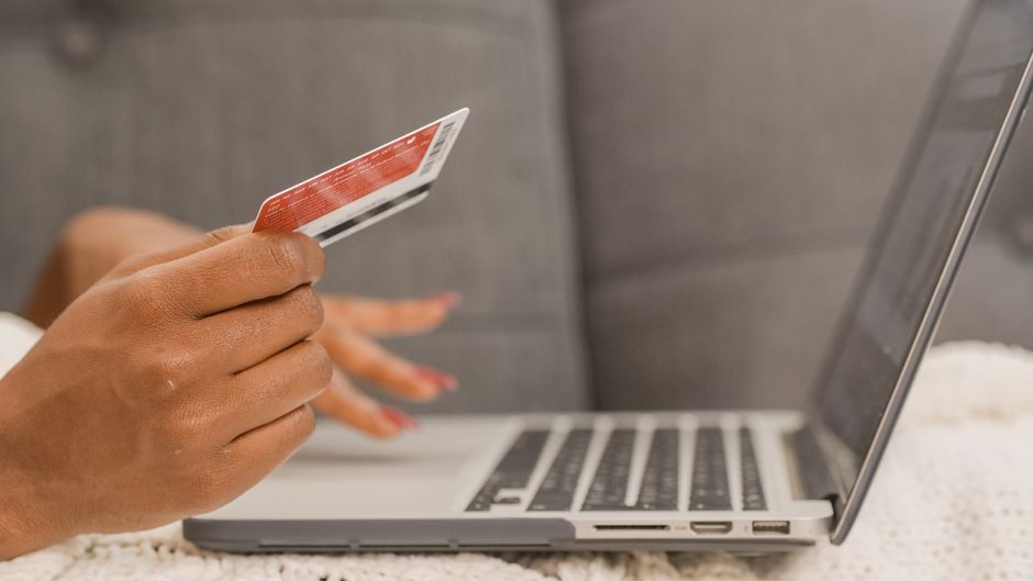Pessoa realizando uma compra online usando um cartão de crédito e um laptop, destacando a cultura de compras digitais.