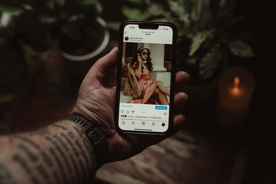 Pessoa segurando um celular exibindo uma foto de uma mulher estilosa sentada em um ambiente sofisticado.
