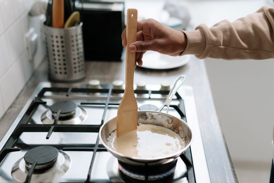 Pessoa cozinhando uma receita em uma panela no fogão, simbolizando preparo e culinária caseira.