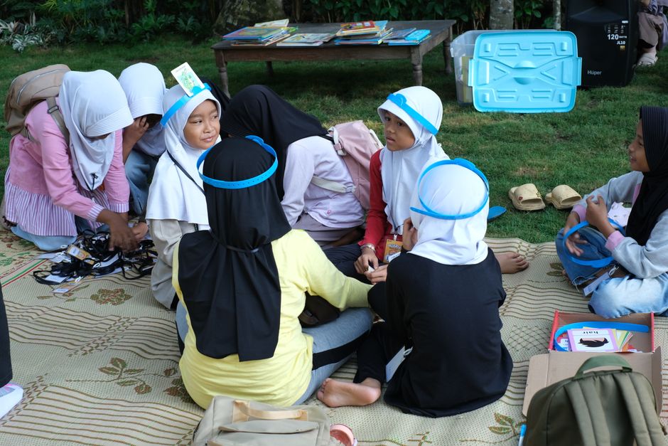 Grupo de crianças participando de atividade educativa ao ar livre, em um ambiente de aprendizagem informal e interativa.