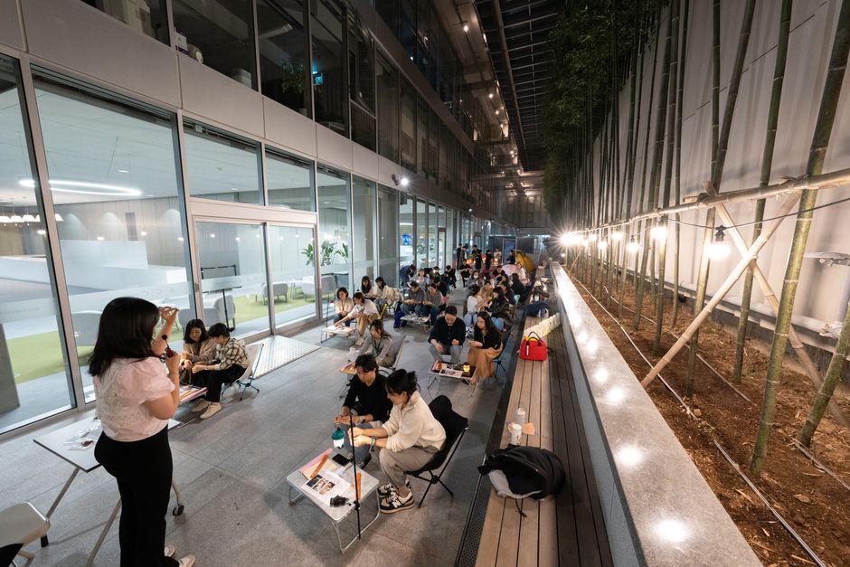 Grupo de pessoas participando de uma atividade de aprendizado ou workshop ao ar livre em ambiente corporativo.