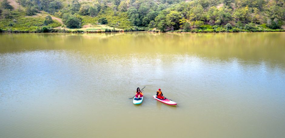 Duas pessoas praticando stand-up paddle em um lago rodeado por natureza, transmitindo tranquilidade e lazer ao ar livre.
