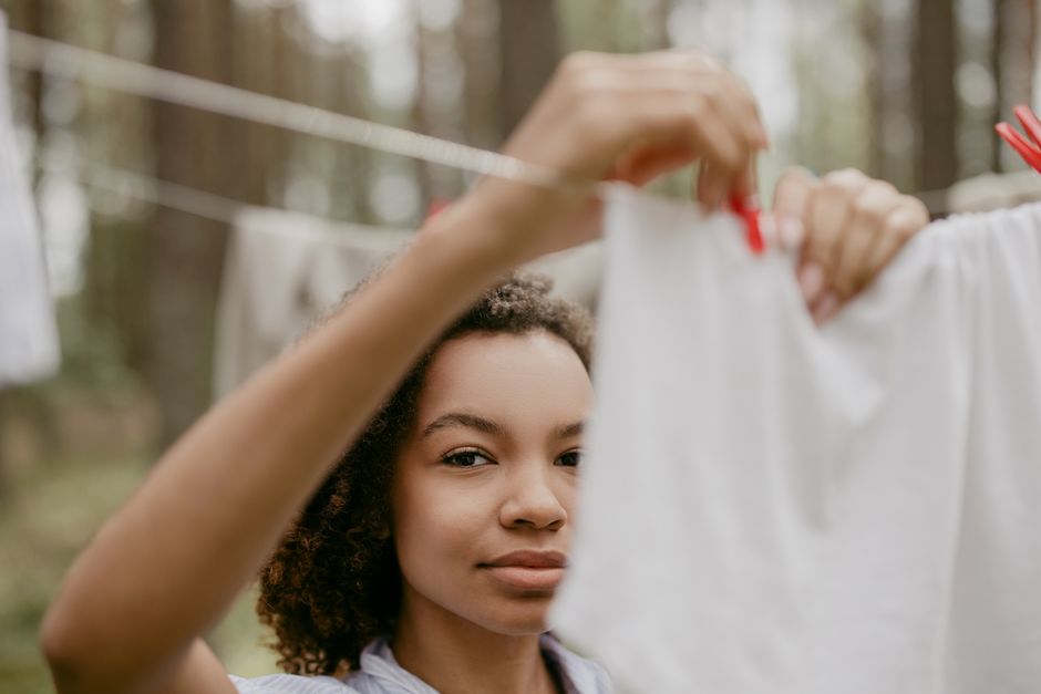 Mulher no ambiente natural pendurando roupas em uma corda de varal ao ar livre.