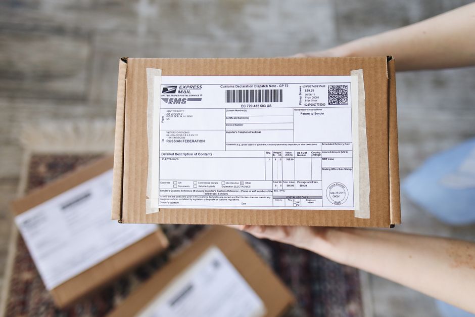 Pessoa segurando uma caixa de remessa com etiqueta de envio internacional, representando logística e comércio eletrônico.