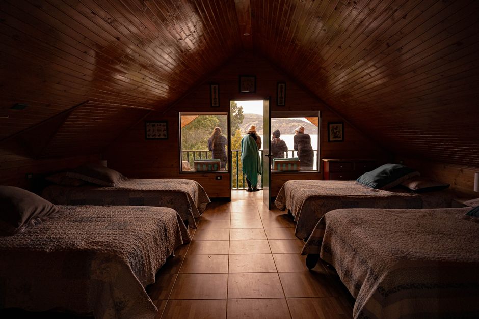 Imagem de um loft com quatro camas de casal, com uma vista de varanda ao fundo por uma porta, criando um ambiente aconchegante e com iluminação natural.