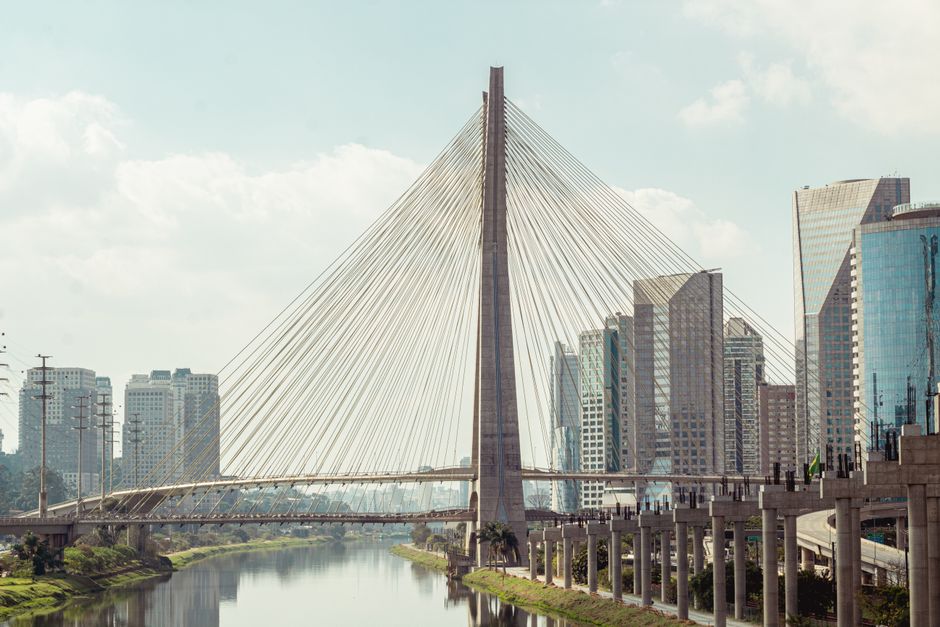 Imagem de uma ponte moderna sobre um rio, com arranha-céus ao fundo, simbolizando conexão e infraestrutura urbana.