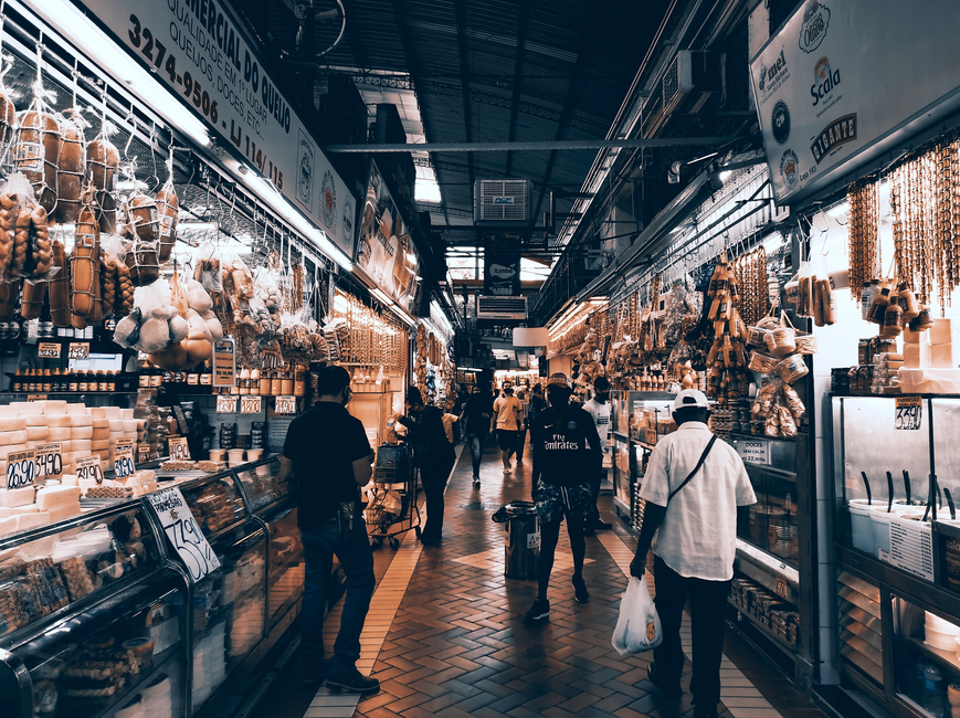 Pessoas fazendo compras em um mercado de alimentos, explorando diferentes produtos nas prateleiras. 