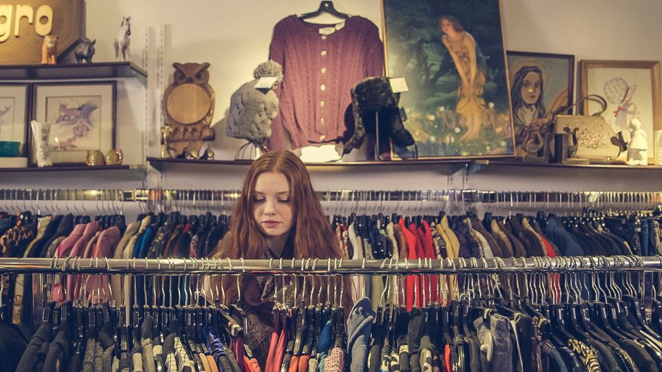Mulher escolhendo roupas em uma loja de roupas vintage, refletindo sobre seu estilo e preferência de moda.