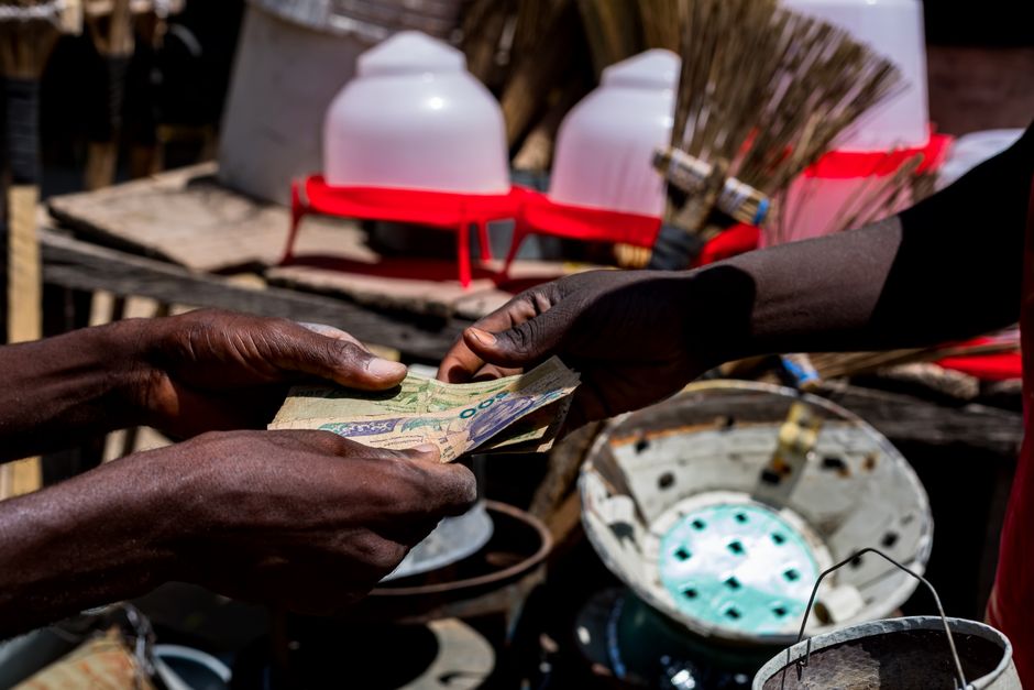 Homem entregando dinheiro manualmente em um ambiente ao ar livre, representando troca ou ajuda financeira em uma comunidade rural.