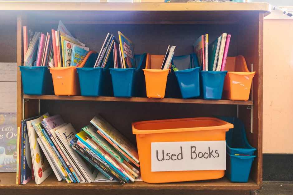 Prateleira de biblioteca com livros usados organizados em caixotes coloridos, ideal para ilustrar dicas de organização e incentivo à leitura.