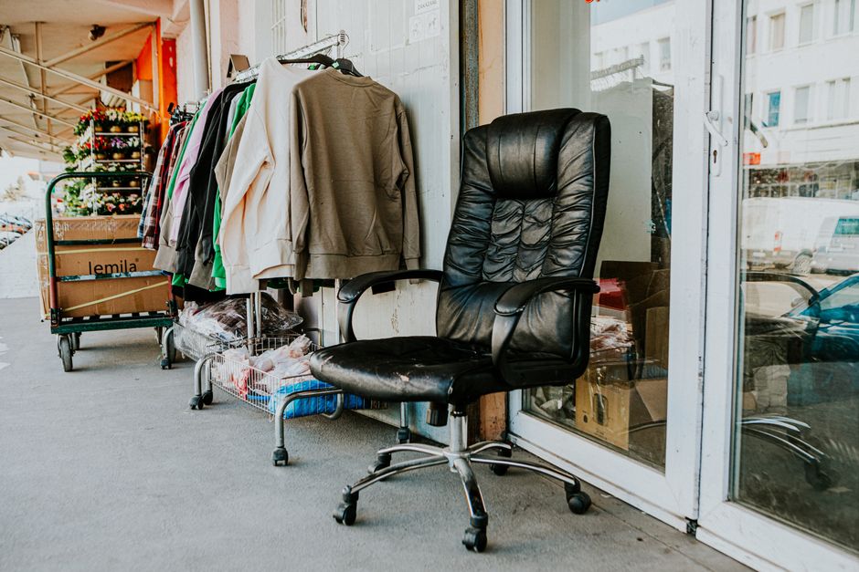 Imagem de uma cadeira de escritório ao lado de uma vitrine com roupas em uma área de vendas, sugerindo um ambiente de comércio ou brechó.