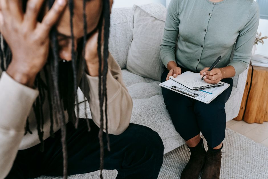 Duas pessoas em uma entrevista de aconselhamento psicológico ou coaching, com uma delas fazendo anotações em um caderno, em um ambiente acolhedor e confortável.