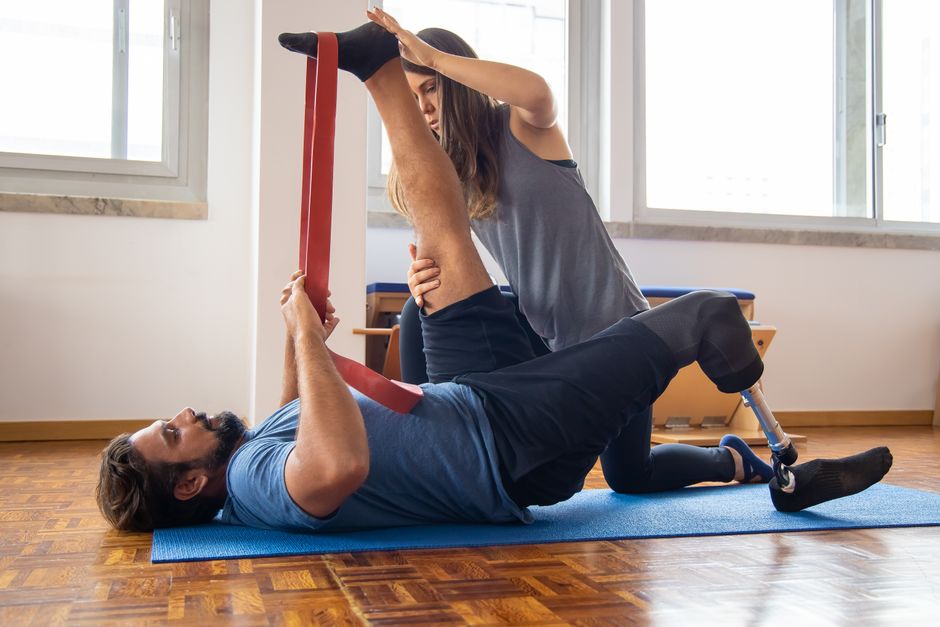 Imagem de uma mulher ajudando um homem com perna amputada a fazer fisioterapia como parte de um exercício de reabilitação ou treinamento físico.