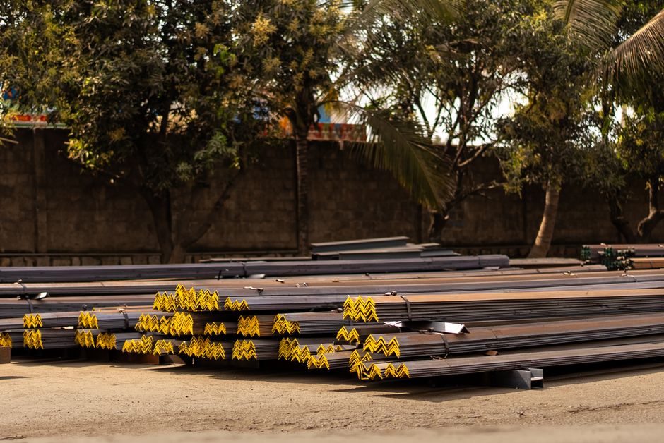 Imagem de caixotes de materiais de construção organizados ao ar livre, com árvores ao fundo, representando logística e armazenamento de matérias-primas para construção civil.
