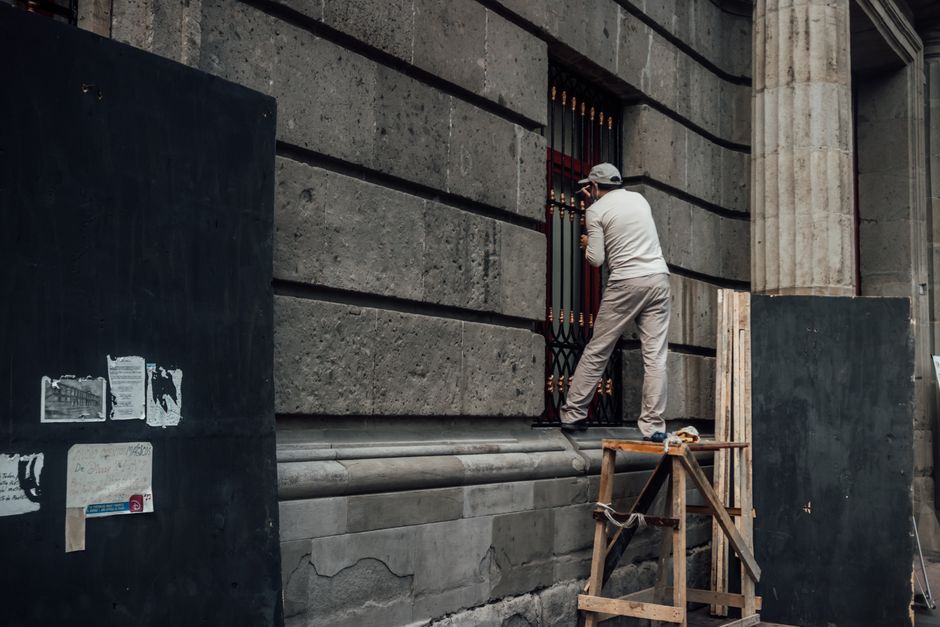 Pessoa utilizando uma câmera para capturar detalhes de uma estrutura arquitetônica de prédio antigo em um ambiente urbano.
