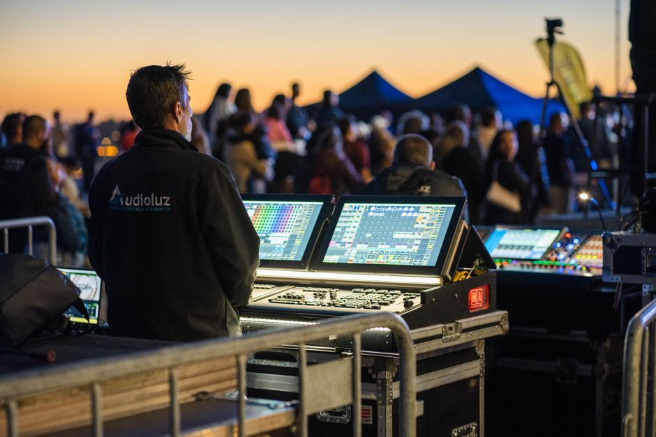 Profissional de tecnologia de eventos controlando a iluminação e sonorização em uma apresentação ao ar livre ao entardecer.
