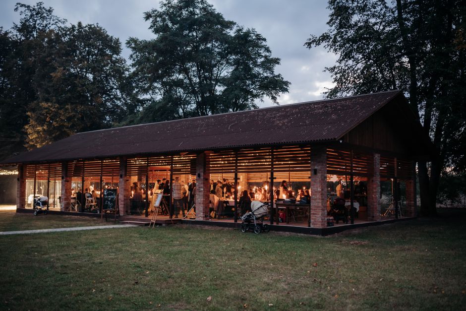 Ambiente de evento ao ar livre com pessoas reunidas dentro de uma estrutura de madeira e vidro ao entardecer.