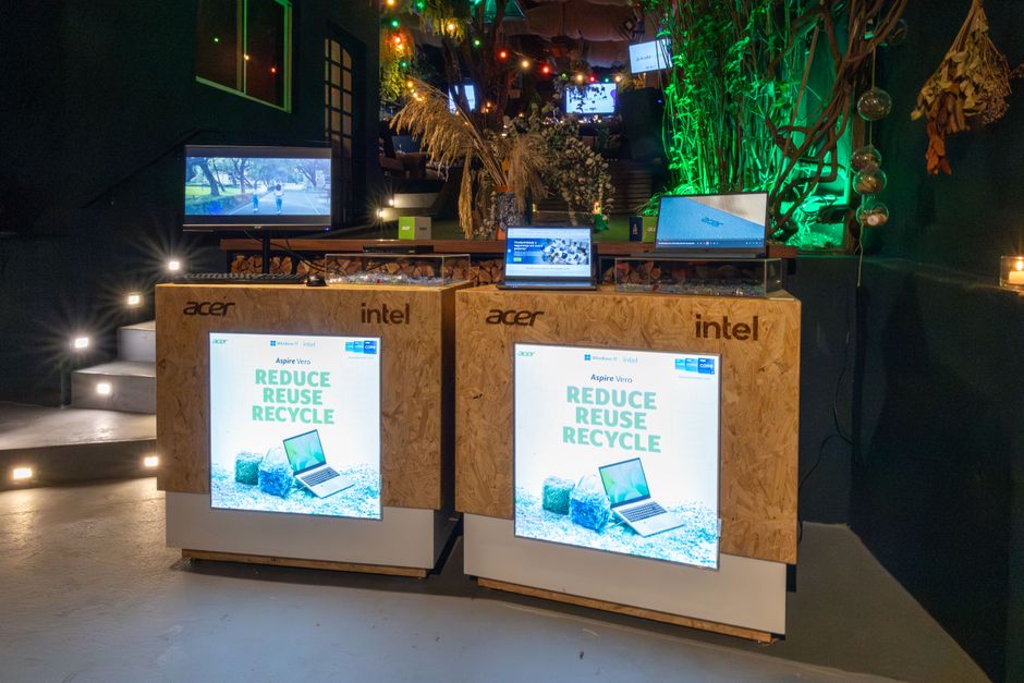 Ambiente moderno de exposição de tecnologia com estandes de computadores e telas digitais, destacando inovação e sustentabilidade.