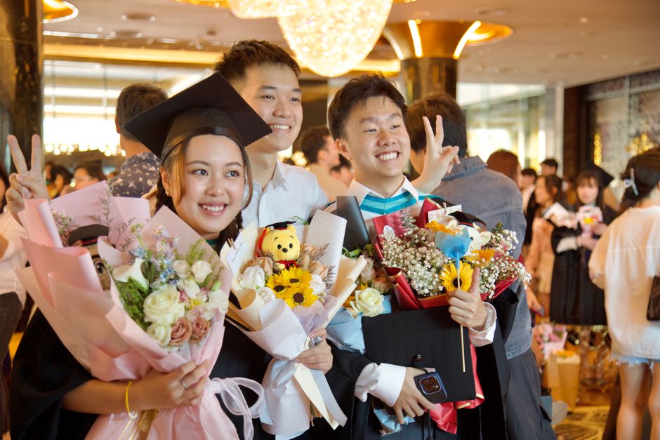 Jovens comemorando formatura com flores, sorrisos e celebração em ambiente festivo.