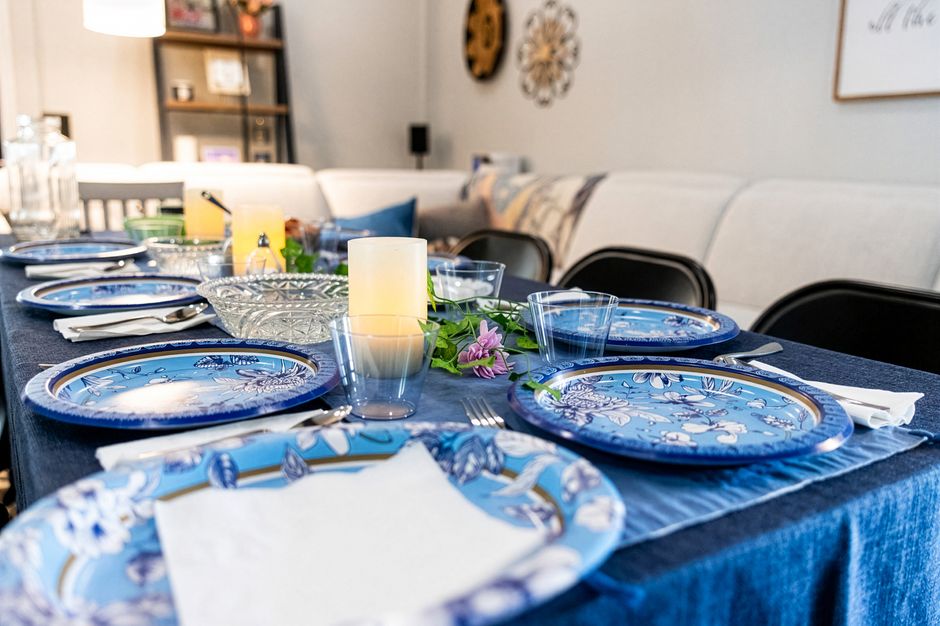 Mesa decorada para um almoço ou jantar, com pratos azuis, velas e arranjo floral, em ambiente acolhedor e elegante.