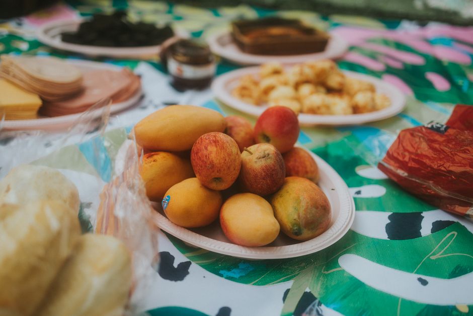 Mesa de festa com frutas variadas e doces, preparando um momento de confraternização ao ar livre.