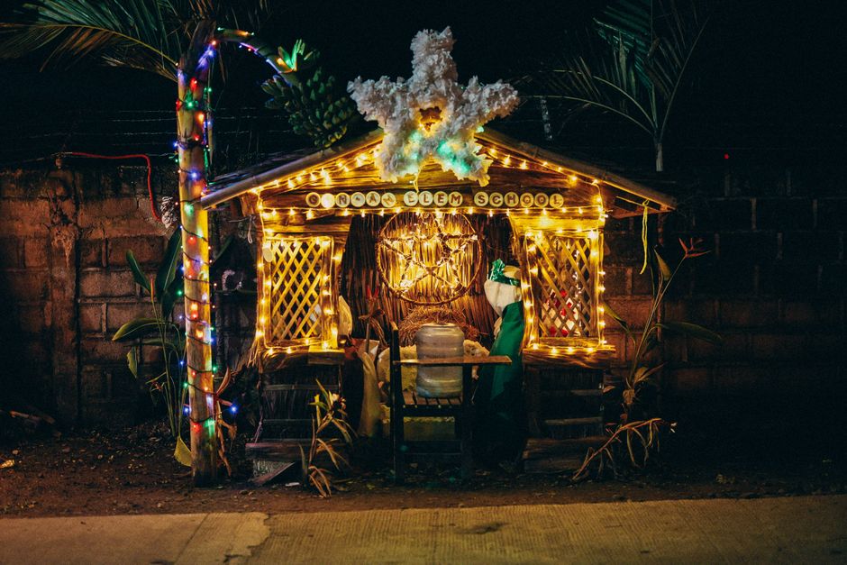 Estrutura decorativa de Natal na frente de uma escola com iluminação colorida, destaque para elementos festivos e ambiente ao ar livre.