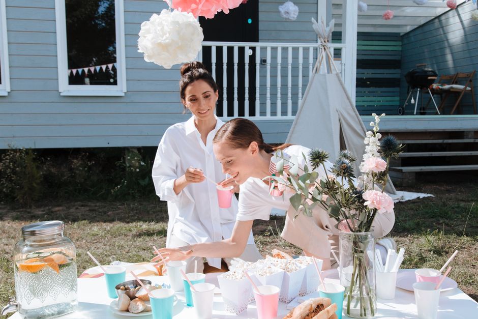Duas mulheres celebrando um momento de confraternização ao ar livre, com decoração delicada e um ambiente de festa infantil.