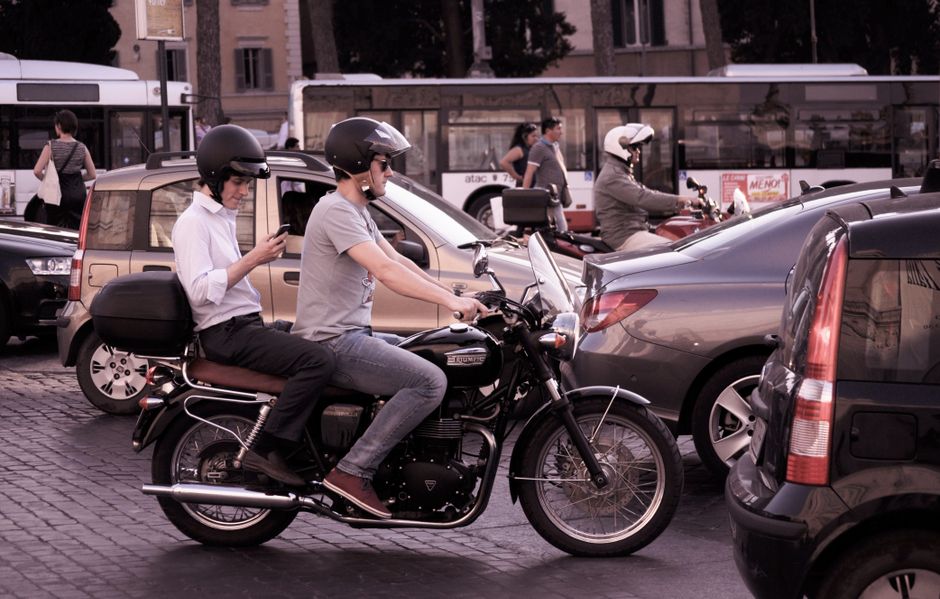 Jovens usando capacetes em uma motocicleta em meio ao trânsito urbano movimentado.