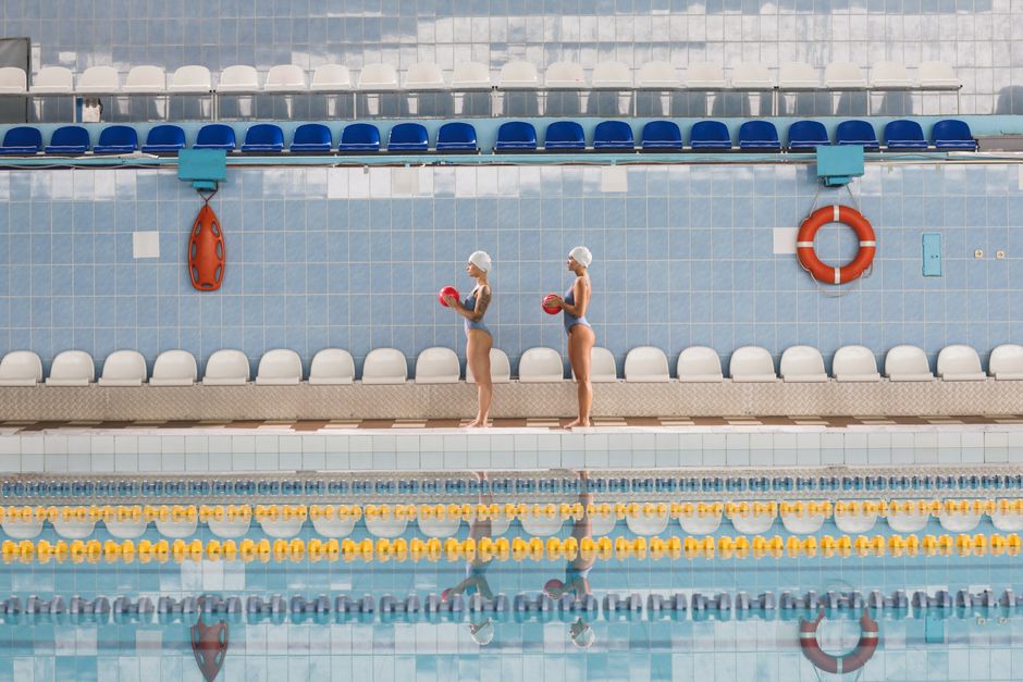Duas nadadoras profissionais descansando na borda da piscina antes de uma sessão de treinamento ou competição.