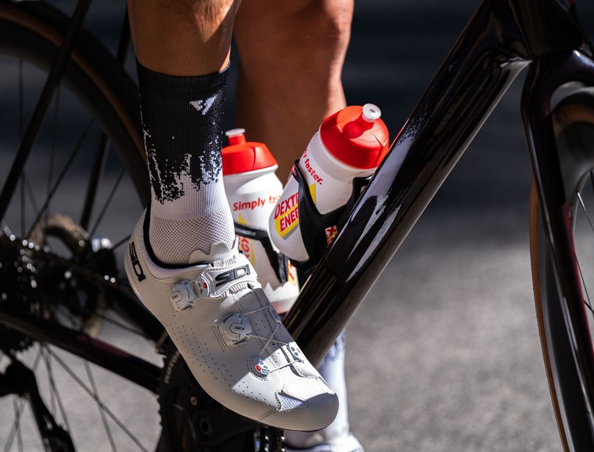 Atleta de bicicleta de estrada ajustando suas garrafas de água, destacando a importância do preparo físico e hidratação para o ciclismo.
