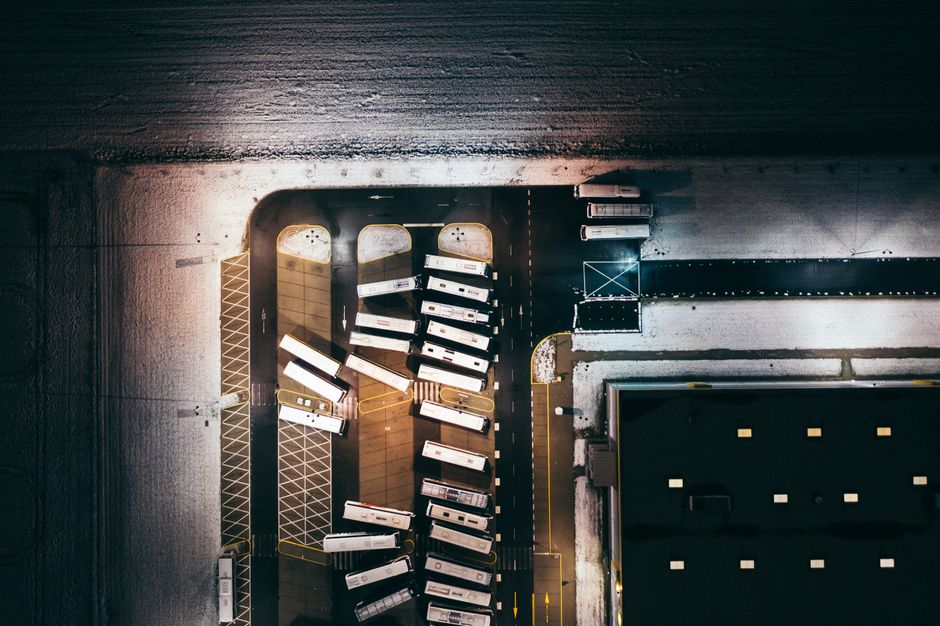 Imagem aérea de um estacionamento com vários ônibus alinhados em um ambiente urbano sob luz suave, podendo ser usada em artigos sobre transporte público ou mobilidade urbana.