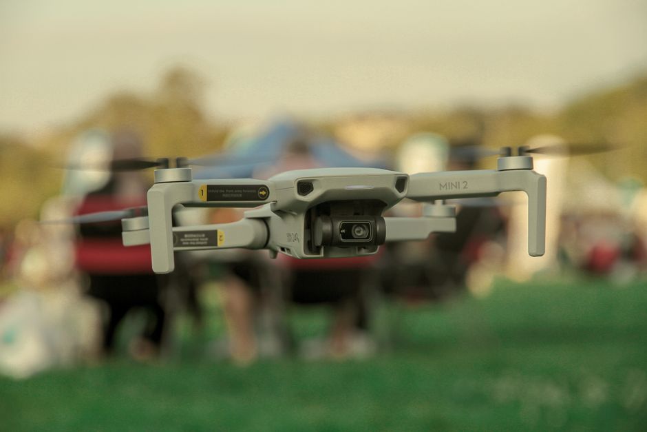 Imagem de um drone em voo com foco na câmera, destaque para tecnologia de filmagem aérea em um evento ao ar livre.