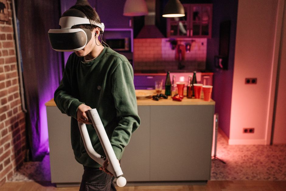 Pessoa usando óculos de realidade virtual em uma festa ou reunião social, com ambiente iluminado e várias bebidas ao fundo.