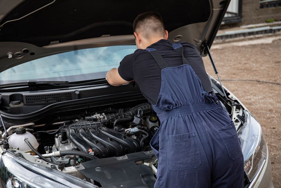 Homem realizando manutenção em carro, inspecionando o motor ao ar livre.