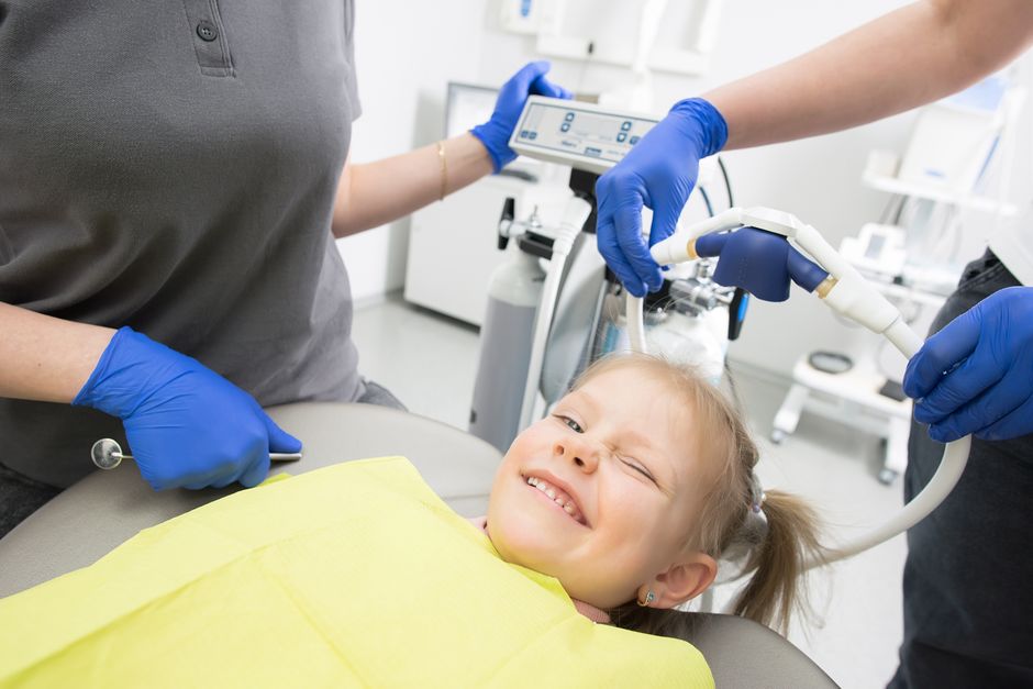 Criança sorridente recebendo atendimento odontológico em clínica especializada, ressaltando cuidado e saúde bucal infantil.
