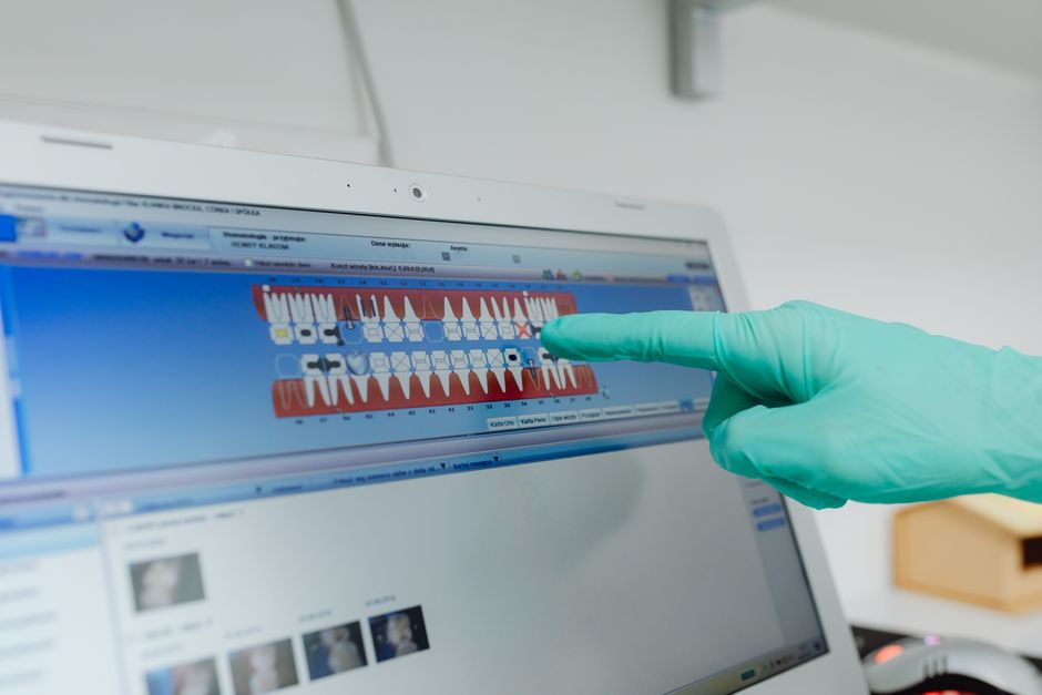 Imagem de um profissional de saúde analisando um resultado de exame odontológico digital em um computador, utilizando luvas de proteção.