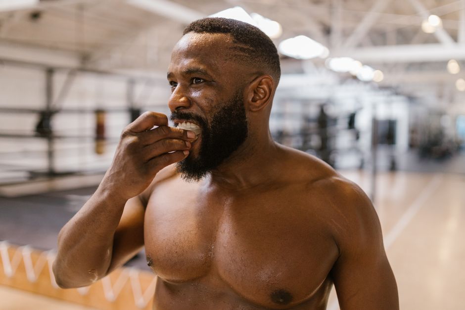 Homem sorridente e sem camisa em ginásio, mostrando satisfação após o treino.