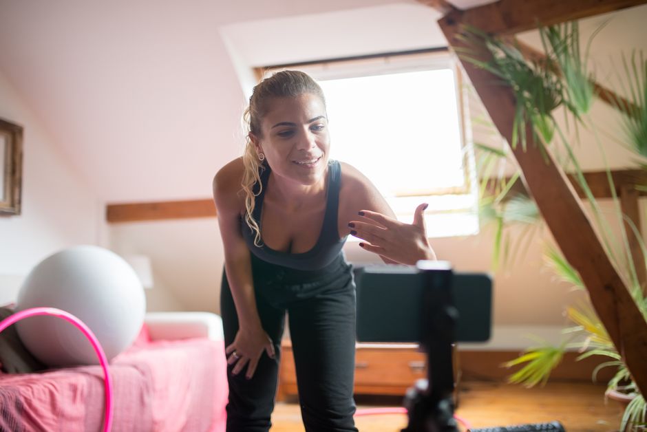 Mulher em casa fazendo uma transmissão ao vivo ou vídeo para blog, com expressão confiante e ambiente acolhedor ao fundo.